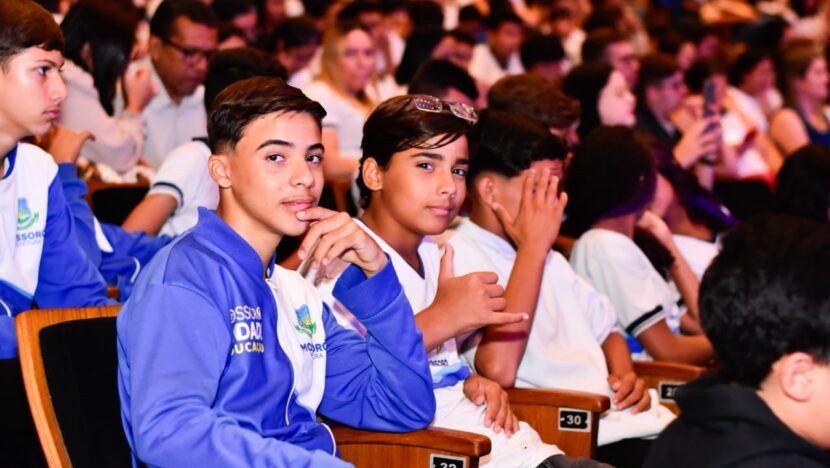 Estudantes com uniforme da rede municipal sentados em auditório durante premiação