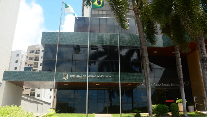Fachada do Tribunal de Contas do Estado do Rio Grande do Norte, com bandeiras e palmeiras em frente ao prédio