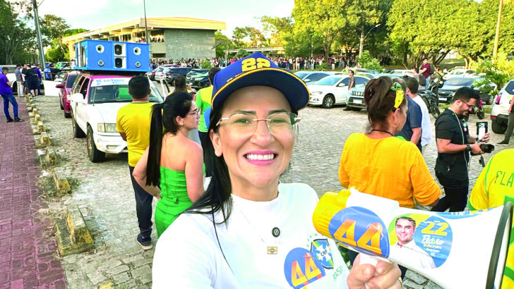 Camila Araújo sorri e faz gesto de positivo durante manifestação, usando camisa com adesivos de campanha