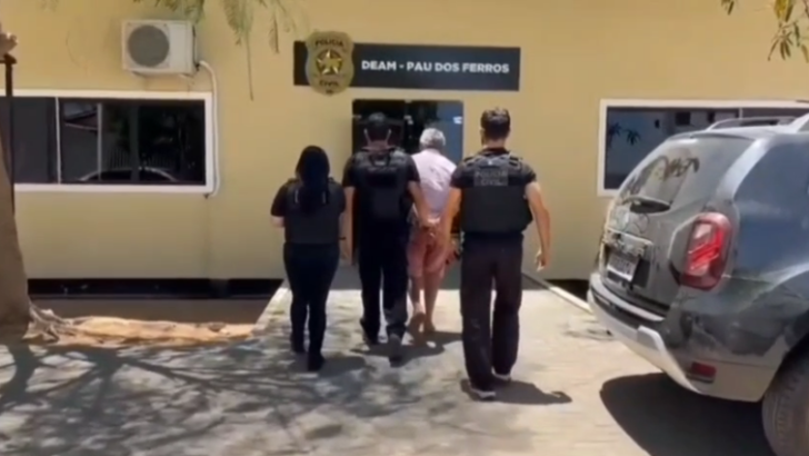 Policiais civis acompanham homem em direção à entrada da Delegacia Especializada de Atendimento à Mulher de Pau dos Ferros