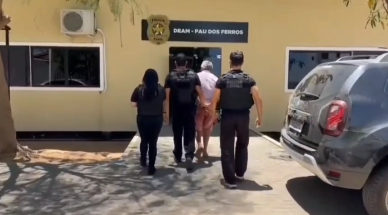 Policiais civis acompanham homem em direção à entrada da Delegacia Especializada de Atendimento à Mulher de Pau dos Ferros