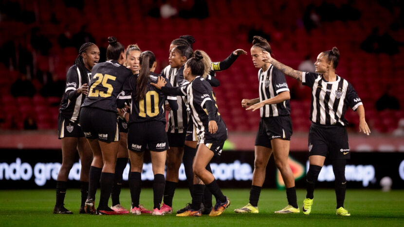 Jogadoras do Atlético-MG, com uniformes listrados em preto e branco, comemoram juntas no gramado do Beira-Rio