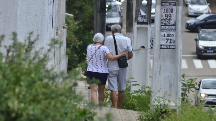 Casal de idosos caminha de costas em área urbana