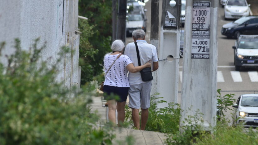 Casal de idosos caminha de costas em área urbana