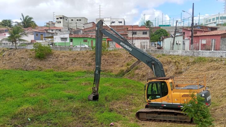 Escavadeira trabalha na limpeza de uma lagoa de captação, cercada por casas em Natal