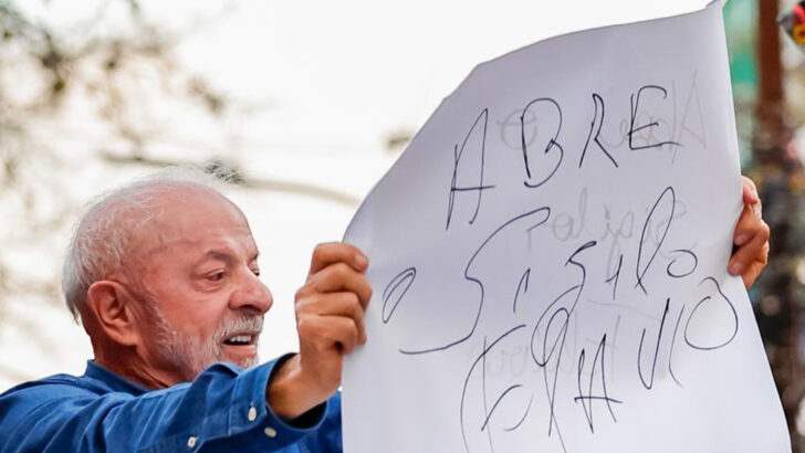 Lula segura um cartaz manuscrito com a frase “Abre o sigilo Flávio” durante ato em Porto Alegre