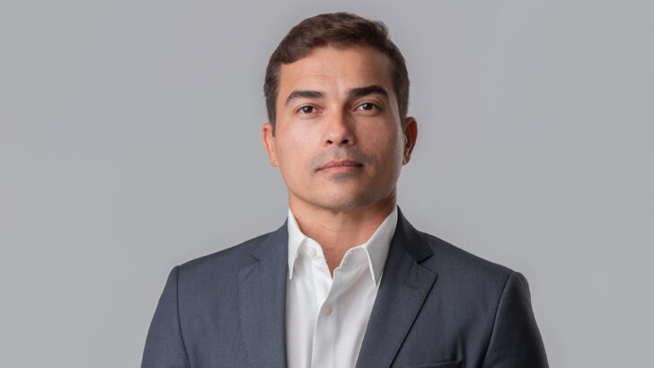 Massimo Chaves posa de frente, com paletó escuro e camisa branca, diante de um fundo cinza.