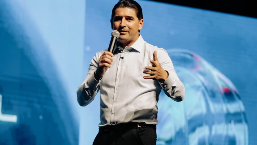 Homem de camisa social segura microfone durante apresentação em um palco