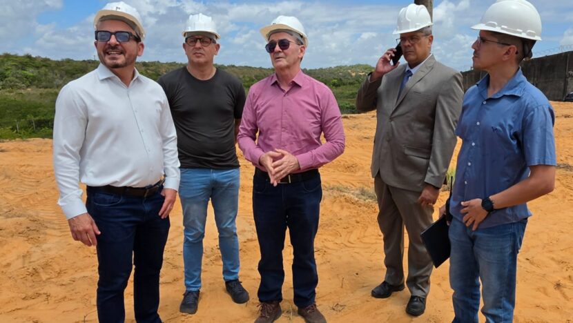 Cinco homens usando capacetes de segurança durante visita a área onde são realizados serviços de construção