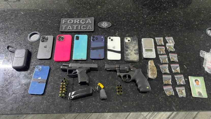 Armas de fogo, munições, celulares, balança e pequenas embalagens dispostos sobre uma bancada escura