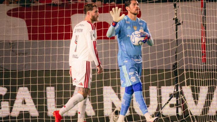 Rossi, de uniforme azul, segura a bola e orienta a equipe ao lado de Léo Pereira, diante da rede do gol