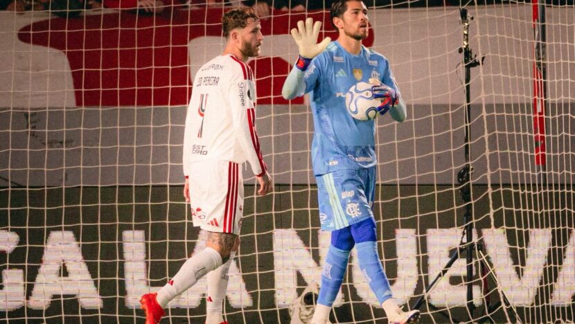 Rossi, de uniforme azul, segura a bola e orienta a equipe ao lado de Léo Pereira, diante da rede do gol