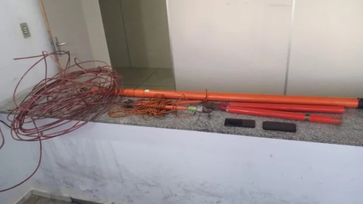 Cabos enrolados, fios e tubos de cor laranja estão dispostos sobre um balcão de granito, ao lado de dois objetos retangulares pretos, em um ambiente fechado