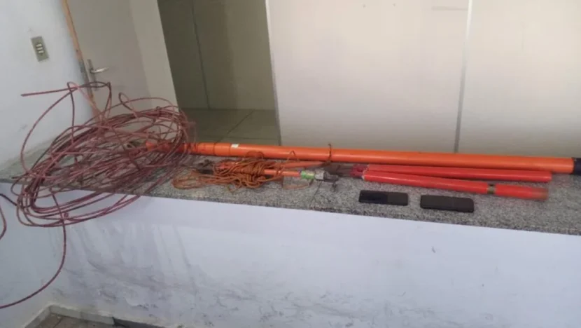 Cabos enrolados, fios e tubos de cor laranja estão dispostos sobre um balcão de granito, ao lado de dois objetos retangulares pretos, em um ambiente fechado