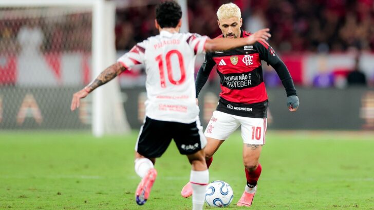 Arrascaeta, com uniforme do Flamengo e proteção no punho, conduz a bola diante de Tiago Palacios