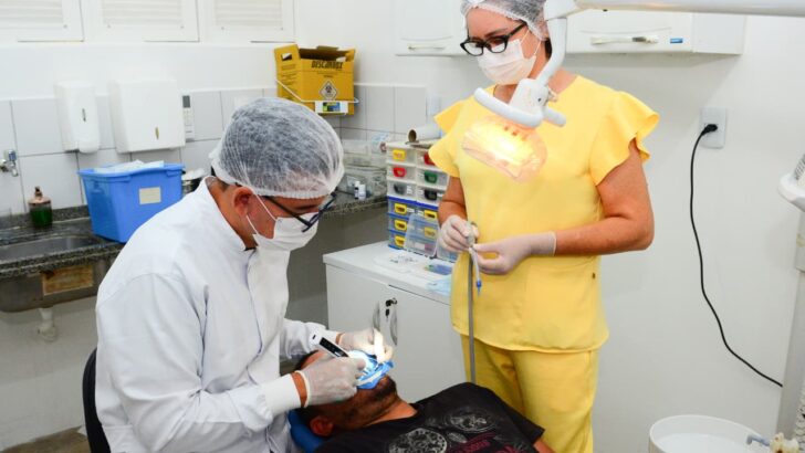 Dentista e auxiliar atendem paciente em consultório odontológico