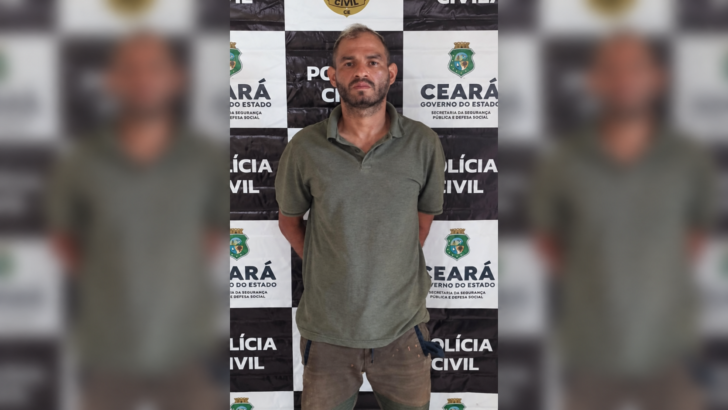 Anderson Stallone, de camisa polo verde e bermuda marrom, diante de painel da Polícia Civil do Ceará, em imagem horizontal com laterais borradas