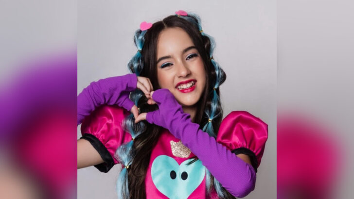 Belinha sorrindo e fazendo um coração com as mãos