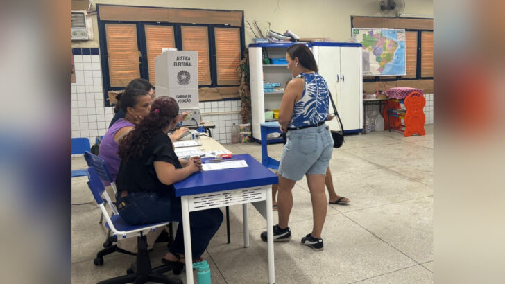 Eleitora diante de mesárias em uma seção eleitoral