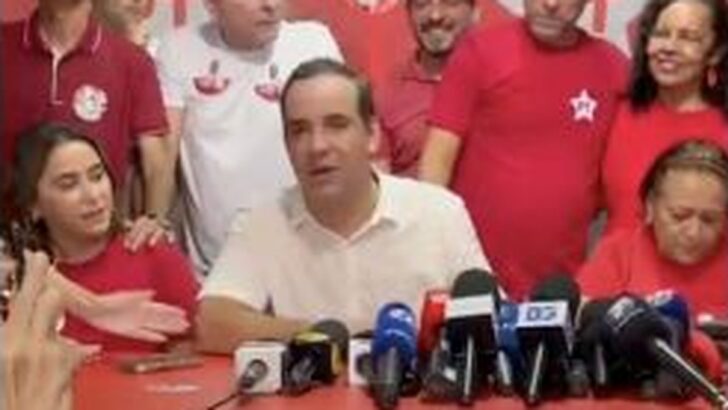 Cadu Xavier diante de microfones, acompanhado de aliados, na coletiva após a vitória em 25 de outubro de 2026