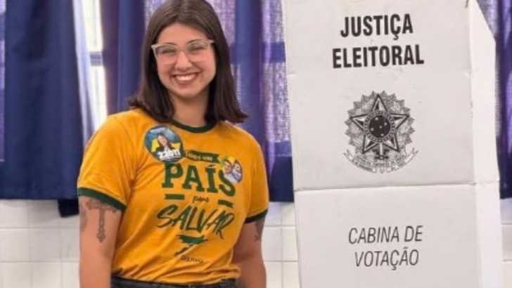 Mulher posa ao lado de uma cabine de votação da Justiça Eleitoral