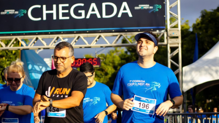 Corredores com camisetas azuis e números de peito passam por estrutura de chegada durante evento esportivo.