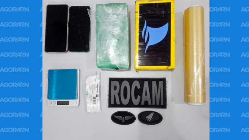 Materiais dispostos sobre uma superfície branca, incluindo dois celulares, dois pacotes retangulares embalados, balança digital azul, embalagens plásticas, rolo de plástico-filme e identificação da Rocam