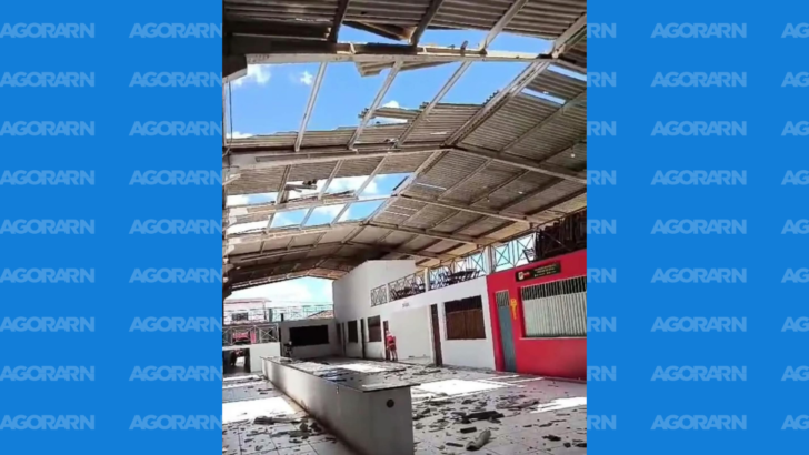 Interior de mercado público com parte das telhas da cobertura arrancada, deixando grandes aberturas por onde é possível ver o céu. Pedaços de materiais estão espalhados pelo piso, próximo aos estabelecimentos comerciais