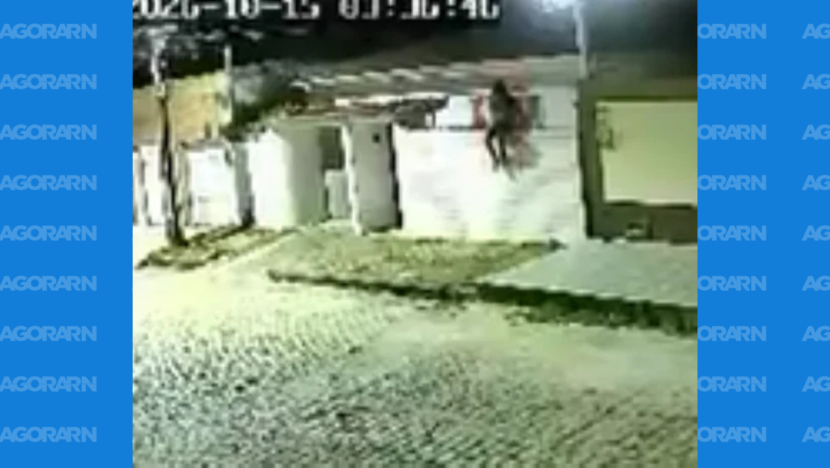 Imagem noturna de câmera de segurança mostra uma pessoa sobre o muro de uma residência em rua de paralelepípedos