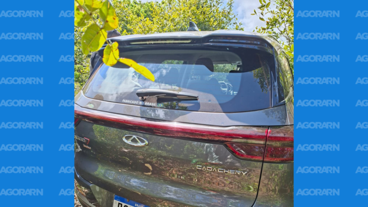 Parte traseira de um SUV Caoa Chery Tiggo 7 de cor cinza-escura, estacionado em área de vegetação, com árvores e arbustos ao redor