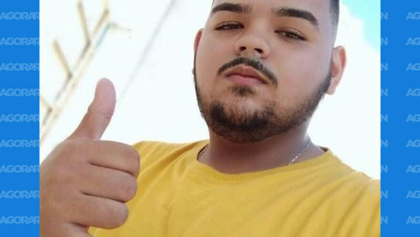 Fotografia de um jovem de cabelo curto e barba, vestindo camiseta amarela, fazendo sinal de positivo com uma das mãos