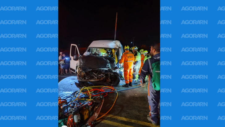 Equipes de resgate trabalham ao redor de um veículo branco com a parte dianteira destruída durante atendimento noturno. Equipamentos hidráulicos e mangueiras estão espalhados sobre a pista