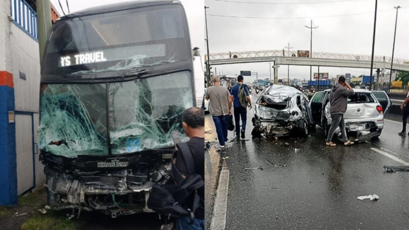 Ônibus de dois andares com a parte frontal destruída e para-brisa estilhaçado aparece ao lado de dois carros com danos graves após acidente em rodovia. Pessoas observam os veículos, enquanto uma passarela aparece ao fundo.
