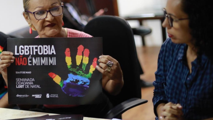 Mulher de óculos segura cartaz com a frase “LGBTfobia não é mimimi”, ao lado de Divaneide Basílio, de blusa azul