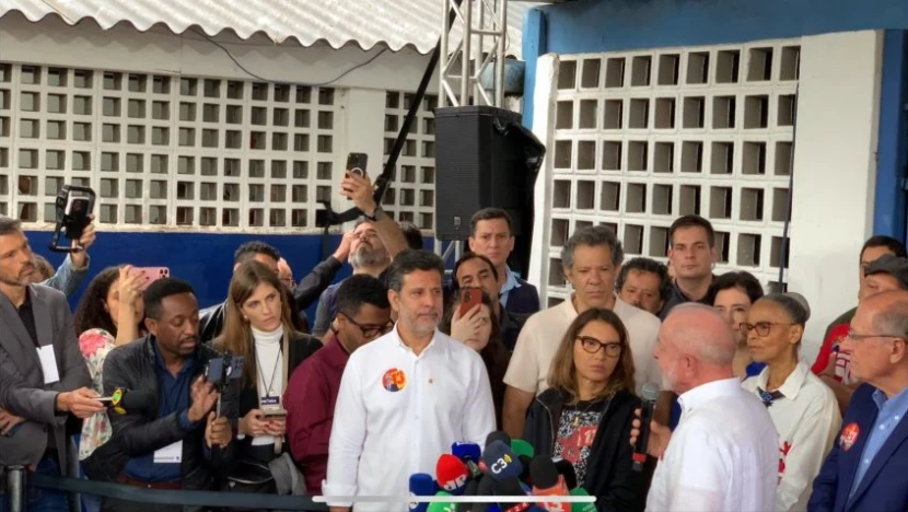Janja ao lado de Lula durante entrevista à imprensa, cercados por jornalistas e aliados após a votação