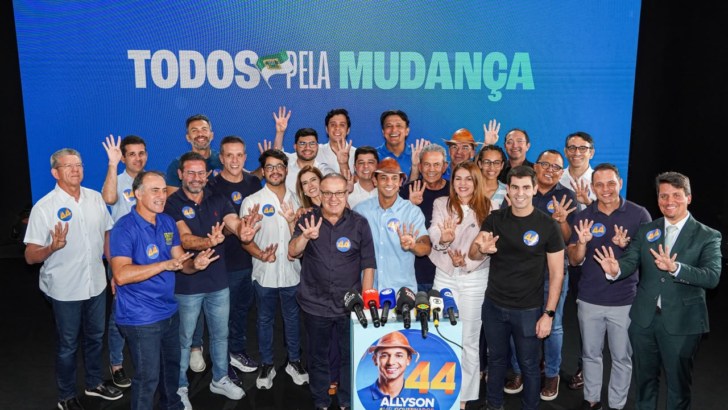 Paulinho Freire, Allyson Bezerra, Nina Souza e aliados posam atrás de microfones, fazendo o gesto do número quatro diante de painel azul com a frase Todos pela mudança