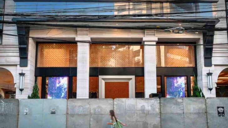 Fachada de prédio com colunas e painéis dourados, sede do Banco Master em São Paulo, fechada por uma barreira de placas de concreto, com um pedestre passando em frente