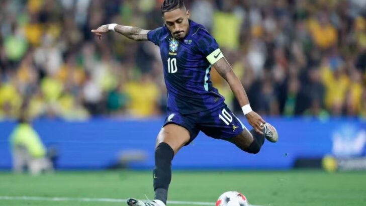 O atacante Raphinha, com a camisa 10 roxa da seleção brasileira e a braçadeira de capitão no braço, no momento do chute à bola