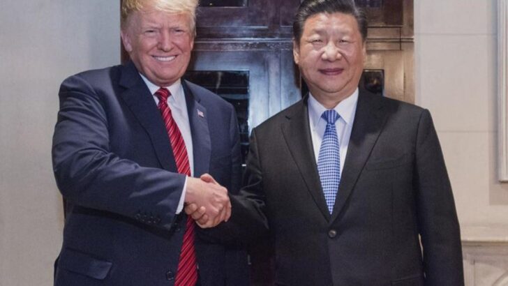 Donald Trump e Xi Jinping, ambos de terno escuro, em pé e apertando as mãos diante das câmeras