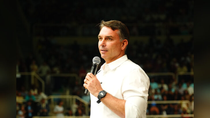 Flávio Bolsonaro, de camisa branca, segura um microfone durante pronunciamento