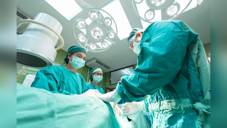 Equipe médica com roupas cirúrgicas verdes atua em sala de cirurgia, sob luminárias