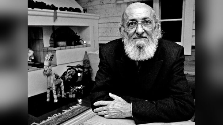 Paulo Freire, de barba branca e óculos, está sentado diante de uma mesa em fotografia histórica em preto e branco