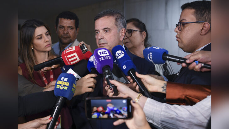 Rogério Marinho, de terno, fala a jornalistas diante de vários microfones