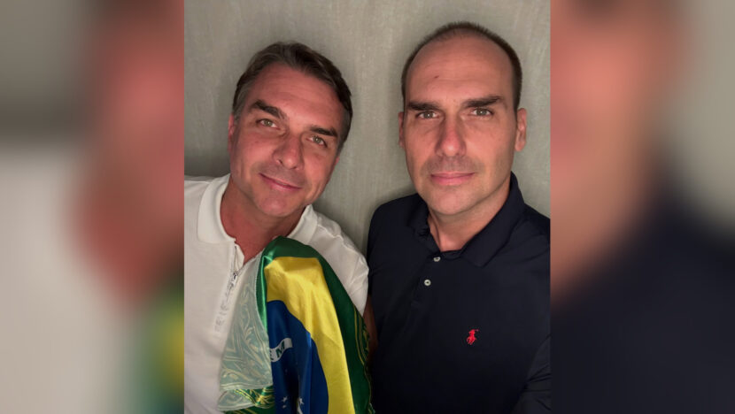 Flávio Bolsonaro ao lado de Eduardo Bolsonaro, com a bandeira do Brasil