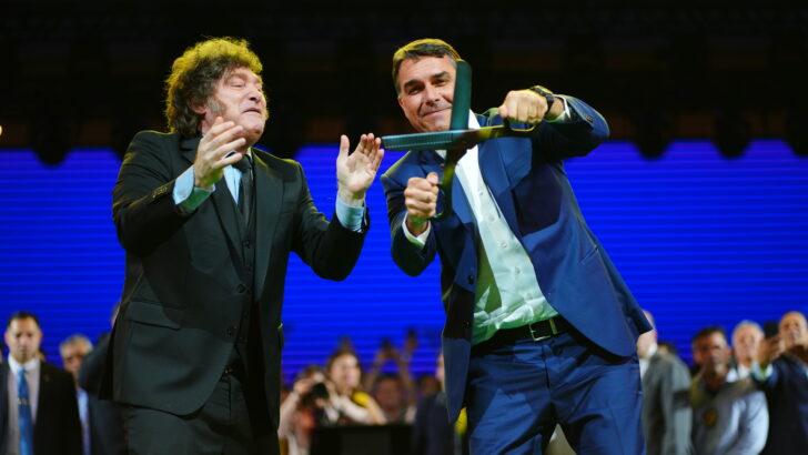 Javier Milei e Flávio Bolsonaro seguram uma motosserra durante encontro