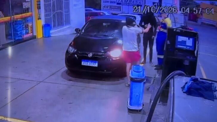 Imagem de câmera de segurança mostra um carro preto parado junto a bombas de combustível, com pessoas próximas ao veículo e à área de abastecimento
