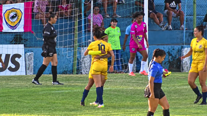 Duas jogadoras do União, de uniforme amarelo, se abraçam diante do gol durante partida contra o Monamy