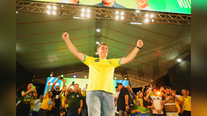 Flávio Bolsonaro com os braços erguidos em evento político