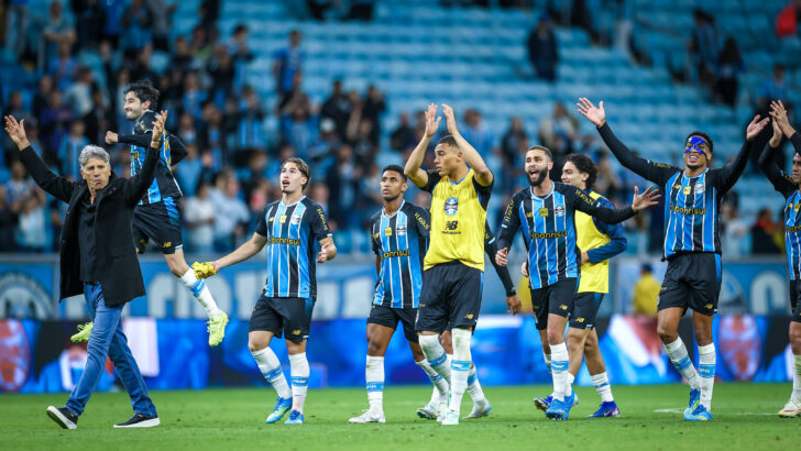Jogadores do Grêmio e integrantes da comissão técnica aplaudem e levantam os braços em direção à torcida no gramado