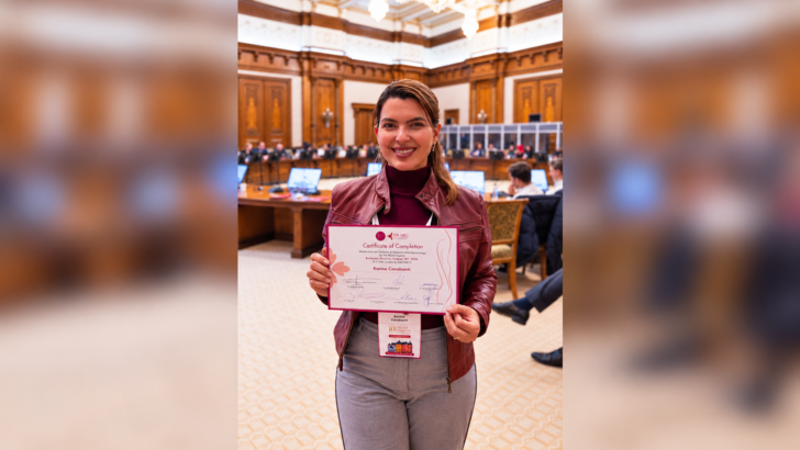 Karina Cavalcanti segura certificado de participação em atividade de ginecologia estética e reconstrutiva, em salão com outros participantes ao fundo